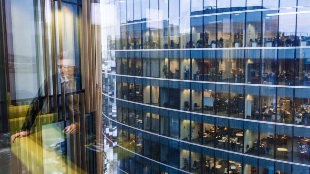 A business man's reflection looking the window onto another office block.